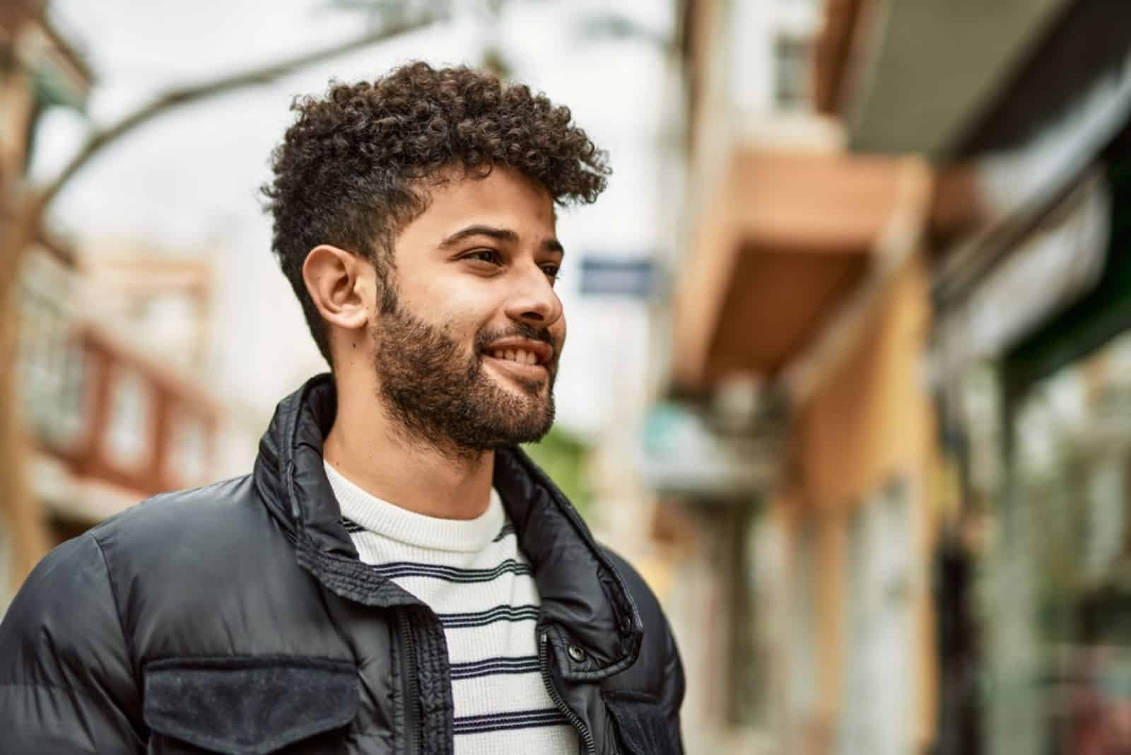 a smiling man with tousled hair is standing on the street