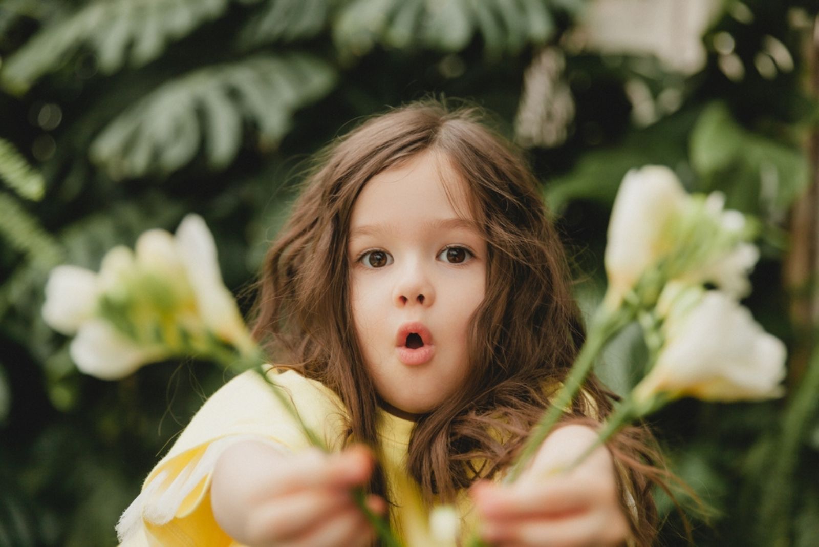 Cute little girl in a yellow dress, holding spring flowers in her hands